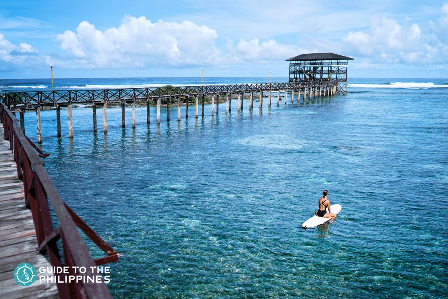 A surfer rests on her board, floating near the iconic Cloud 9 surf break in Siargao Island. A surfer rests on her board, floating near the iconic Cloud 9 surf break in Siargao Island.
