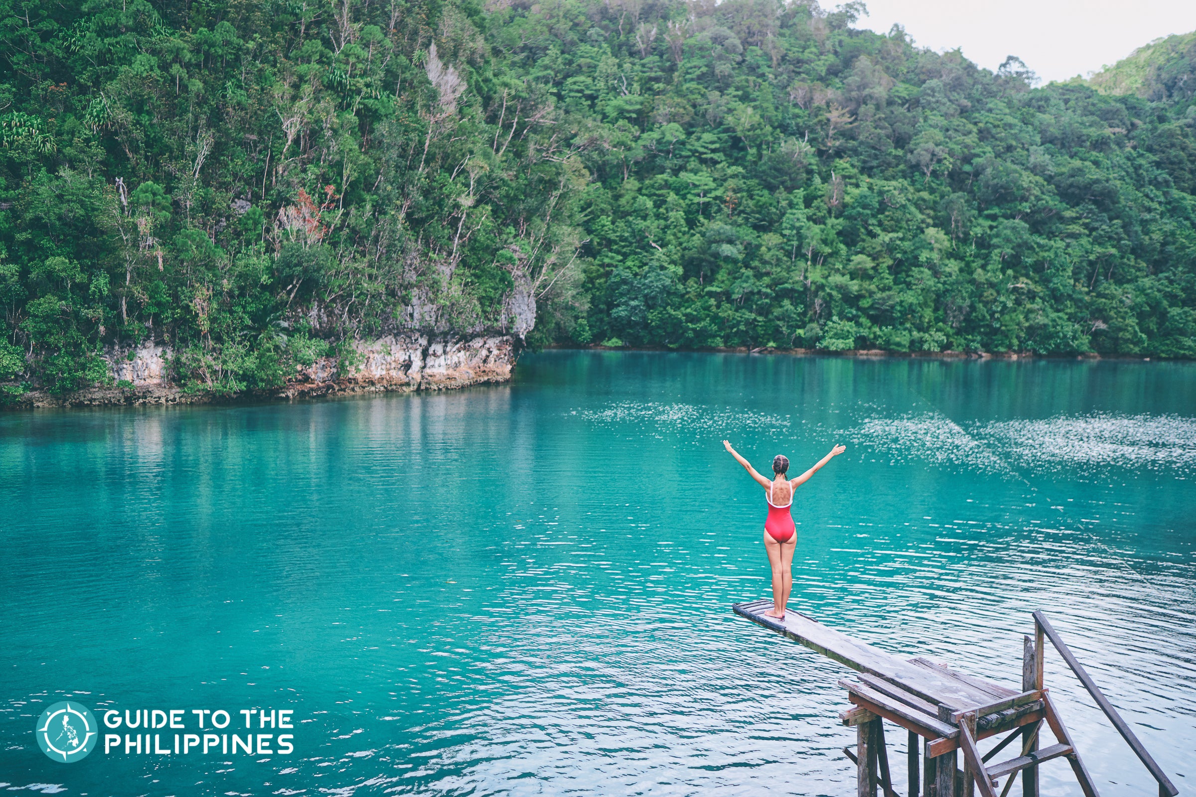 A tourist enjoying the blue tropical lagoon view in Sugba while sitting on its famous wooden springboard.