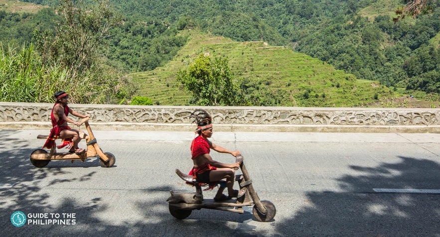 Ifugaos passing by Banaue Rice Terraces on their wooden scooters Ifugaos passing by Banaue Rice Terraces on their wooden scooters