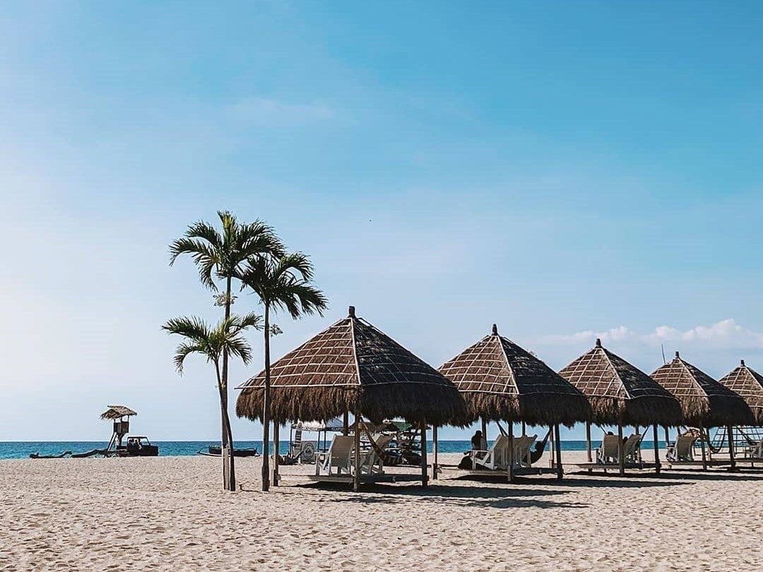 Guest relax under huts on Crystal Beach Resort's beachfront