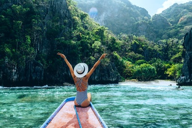 Back view of the young woman in hat relaxing on the boat and looking at the island. Travelling tour in Asia: El Nido, Palawan, Philippines.