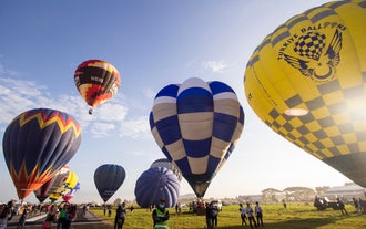 A cluster of colorful hot air balloons ascending at sunrise, seen with this ticket to the Philippine International Hot Air Balloon Festival in New Clark City.