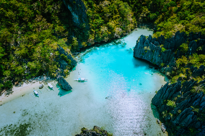 An aerial view of Cadlao Lagoon showcases its crystal-clear blue waters surrounded by towering rock cliffs, a highlight of this island hopping tour D in El Nido town