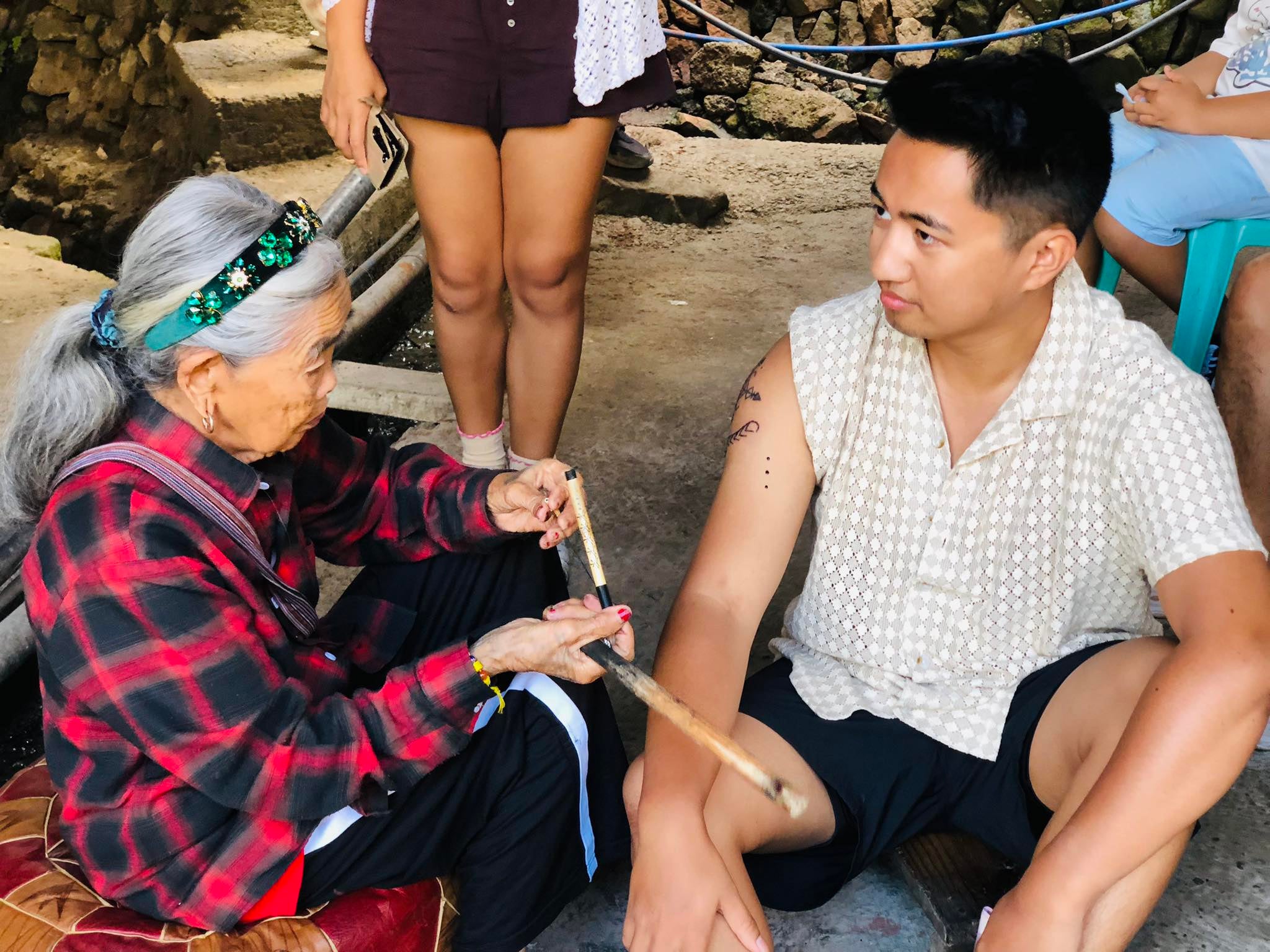 Apo Whang-Od carefully hand-taps a traditional tattoo onto a tourist's arm, a highlight of this Buscalan village tour package