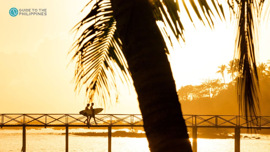 Surfers walking on Cloud 9 boardwalk during sunset in Siargao Surfers walking on Cloud 9 boardwalk during sunset in Siargao