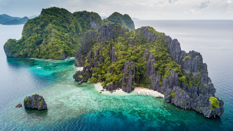 Aerial view of El Nido in Palawan, Philippines, showing a turquoise waters, a white sand beach, towering green limestone cliffs surrounded by island-dotted seas. Aerial view of El Nido in Palawan, Philippines, showing a turquoise waters, a white sand beach, towering green limestone cliffs surrounded by island-dotted seas.